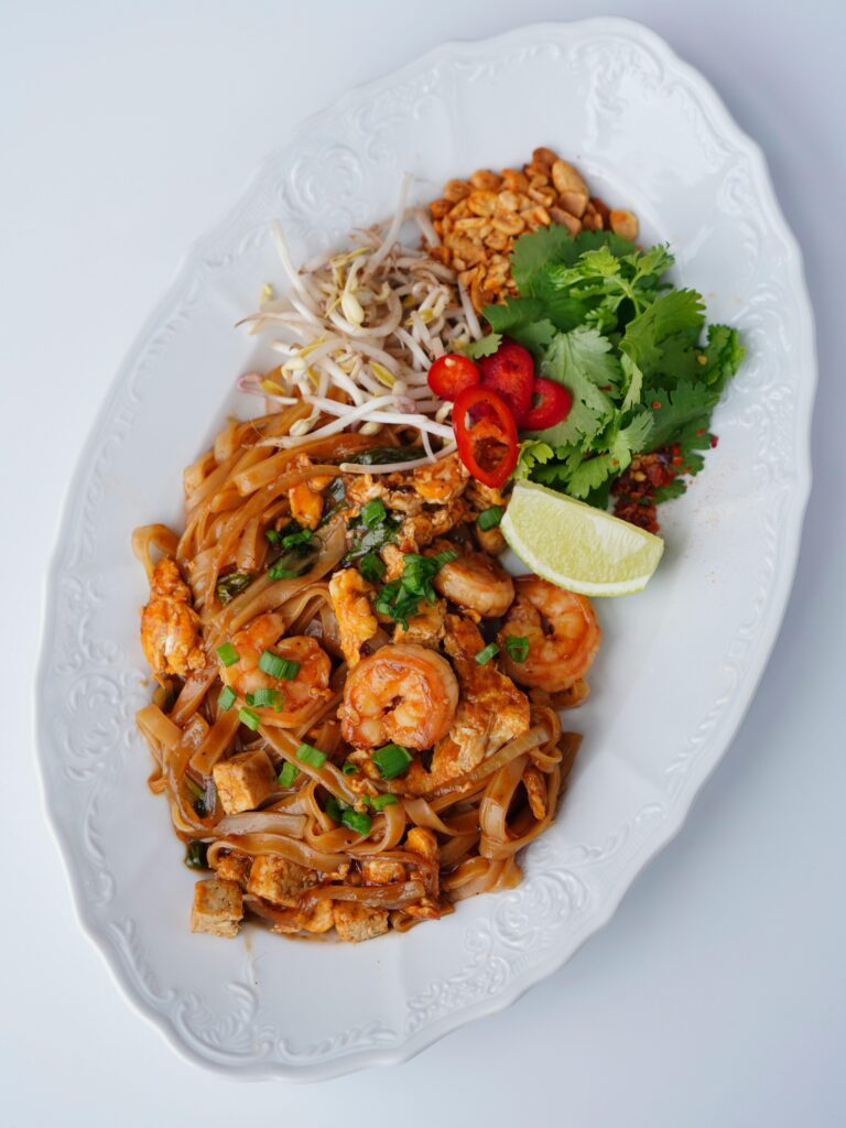 Appetizing Pad Thai with shrimp, peanuts, and fresh herbs on a white plate.